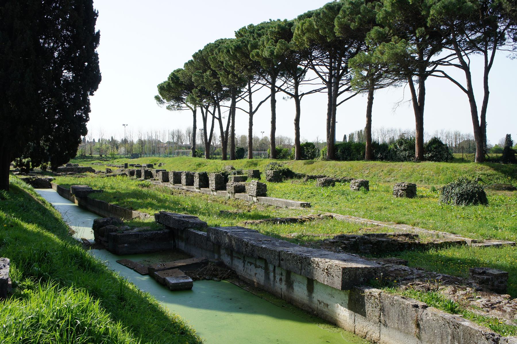 Stone quays of Aquileia's Roman river port beneath umbrella pines