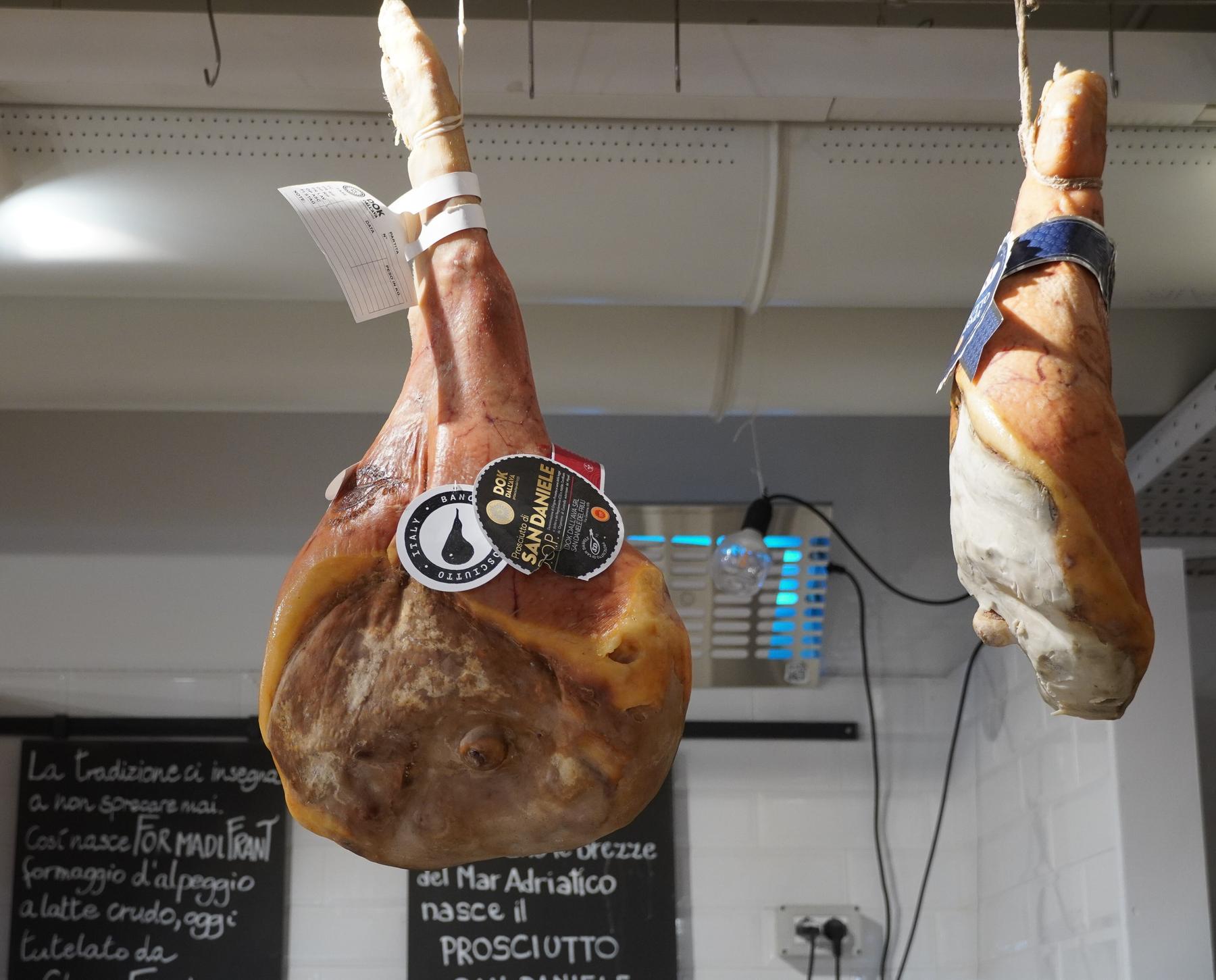 Whole Prosciutto di San Daniele hams hanging with their branded seal