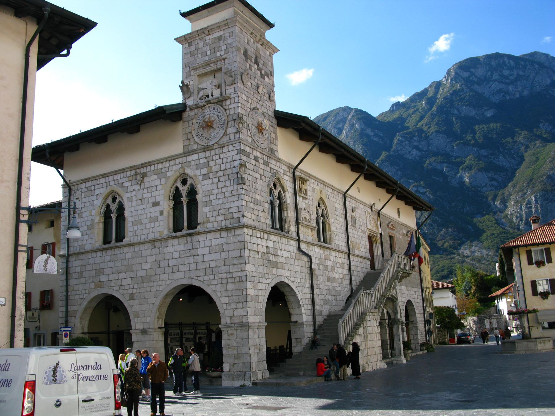 Gothic stone town hall with loggia and clock tower against Alpine peaks